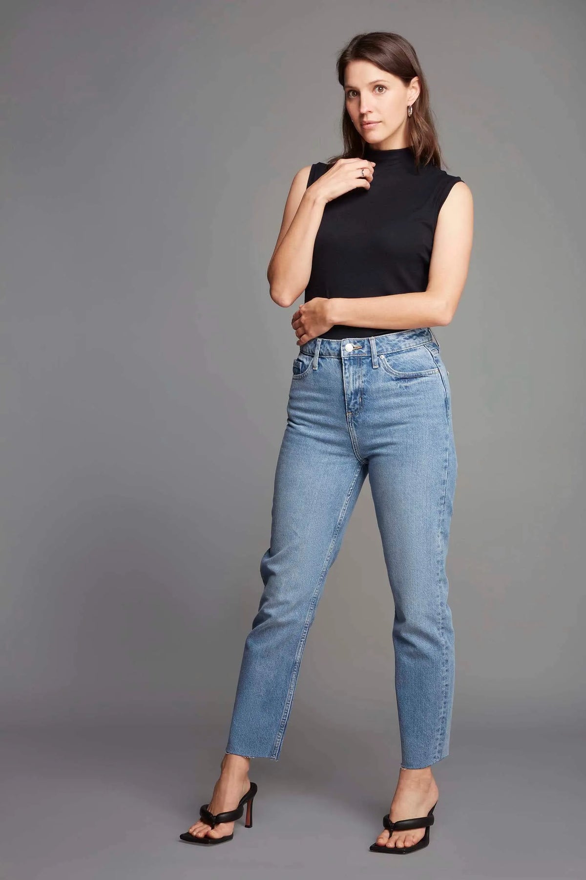 Woman wearing blue jeans and a black top against a gray background