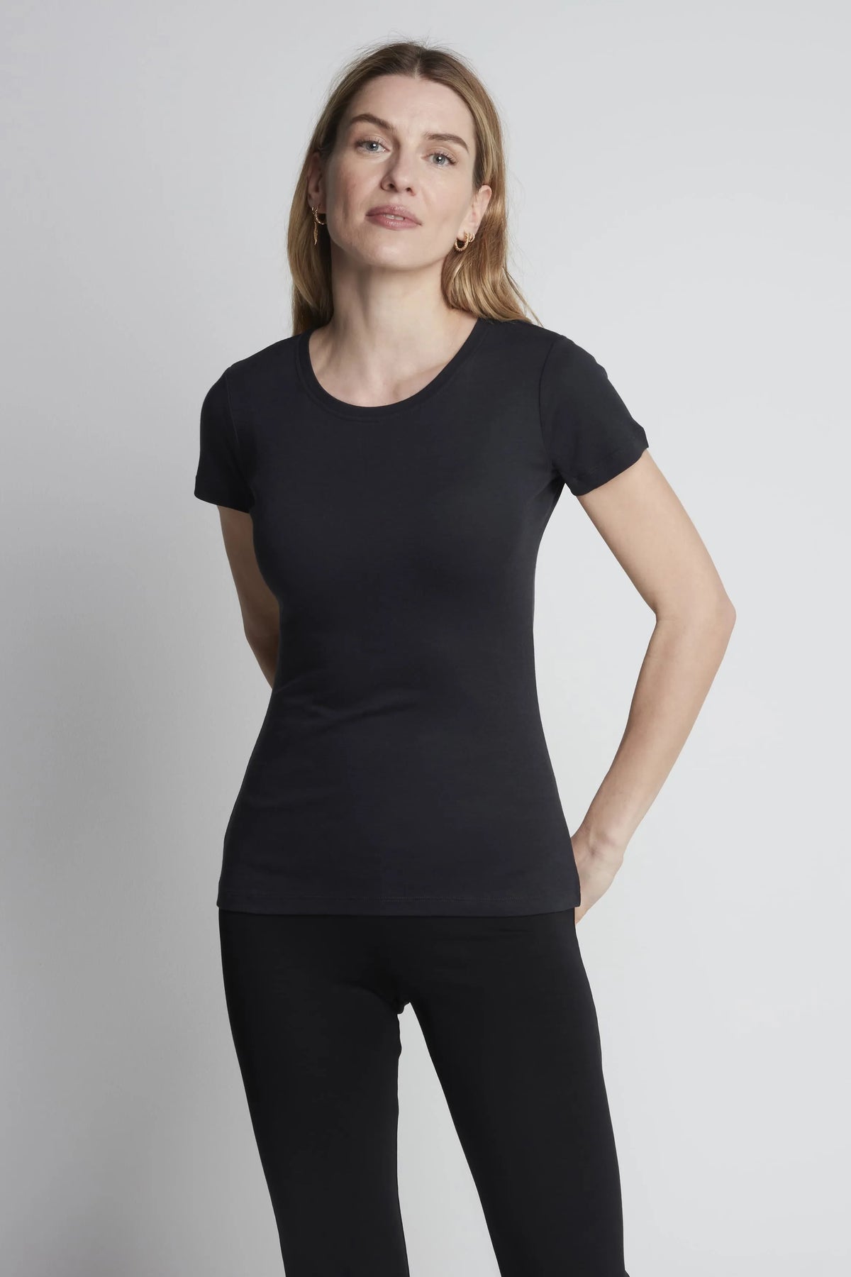 Woman wearing a black t-shirt and black leggings against a plain background