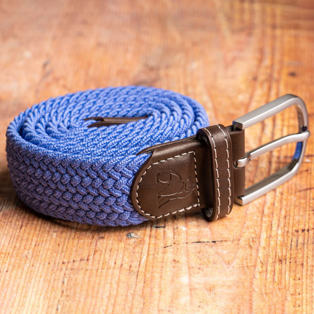 Blue braided belt with a brown leather buckle on a wooden surface